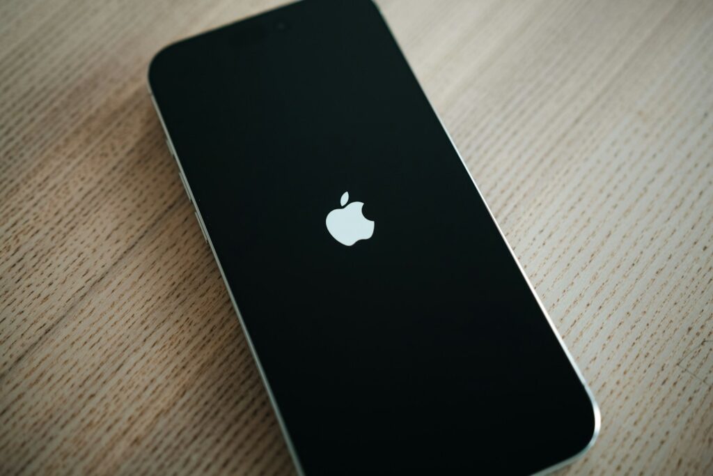 A sleek, minimalistic shot of an iPhone 16 Pro Max box resting on a light wooden surface. The packaging design is modern, with soft lighting enhancing the curves and color of the phone display on the box. The muted tones evoke a clean, tech-focused aesthetic.