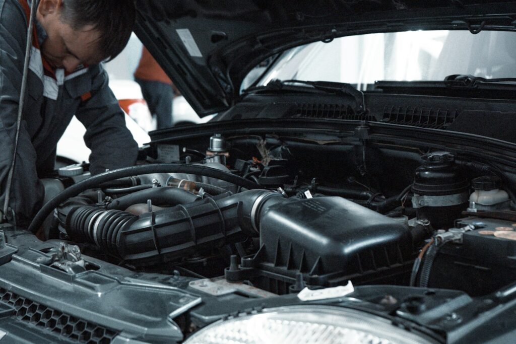 A mechanic in a grey uniform inspecting the engine of a car