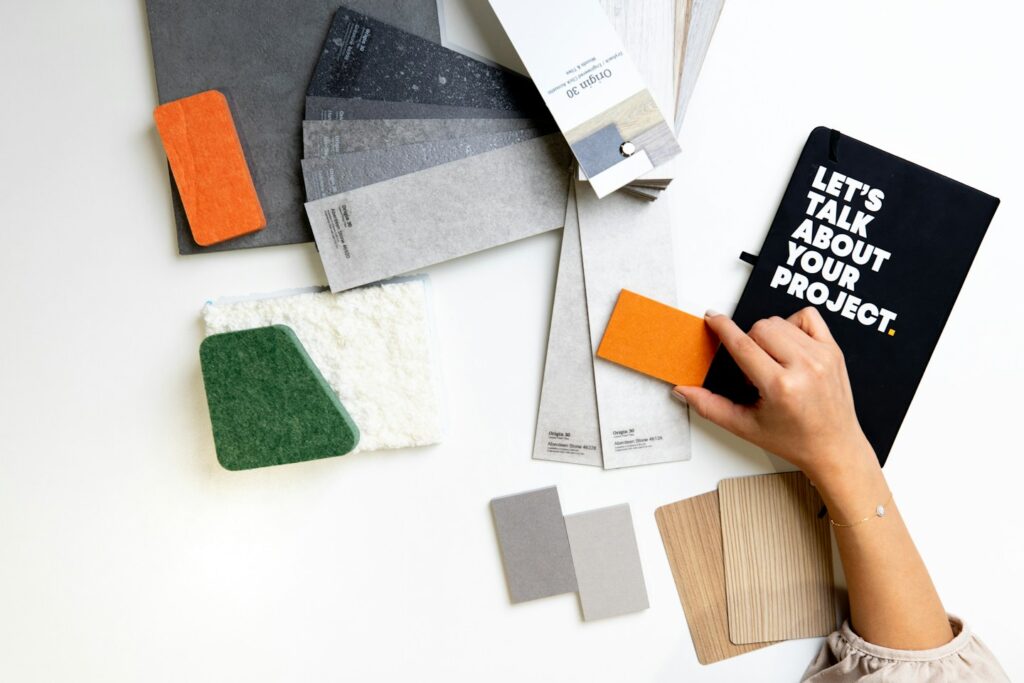 A person holding an orange material sample over a white desk with design swatches