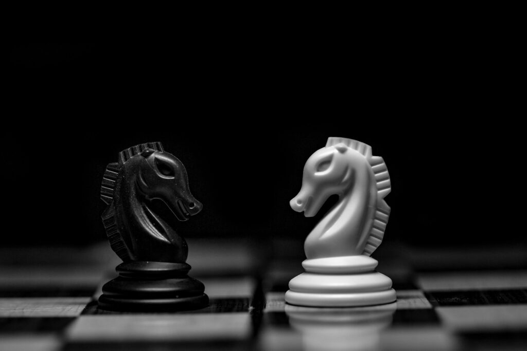 A black and a white chess knight facing each other on a board